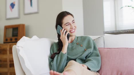 Happy-caucasian-woman-sitting-on-couch-and-talking-on-smartphone