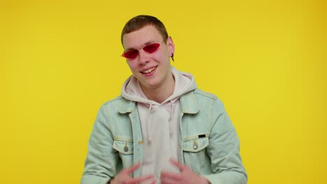 Seductive-cheerful-stylish-man-in-denim-jacket-wearing-sunglasses,-charming-smile-on-yellow-wall