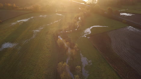 aerial view of a commuter train passing through a english landscape over the river stour with a beautiful sunrise glow