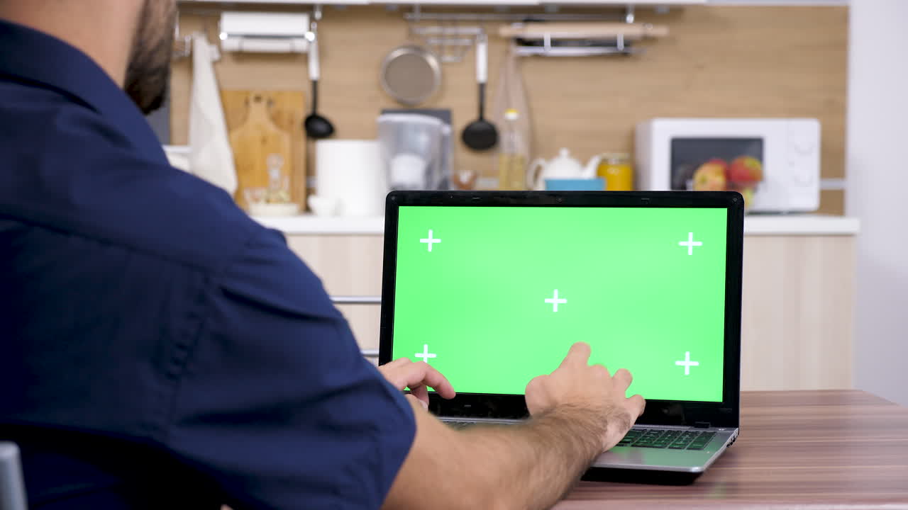 Man working on a laptop with green screen in the kitchen