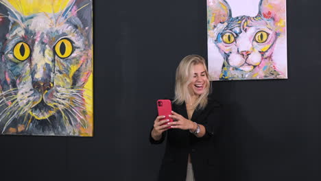 mujer tomando una selfie frente a pinturas de gatos