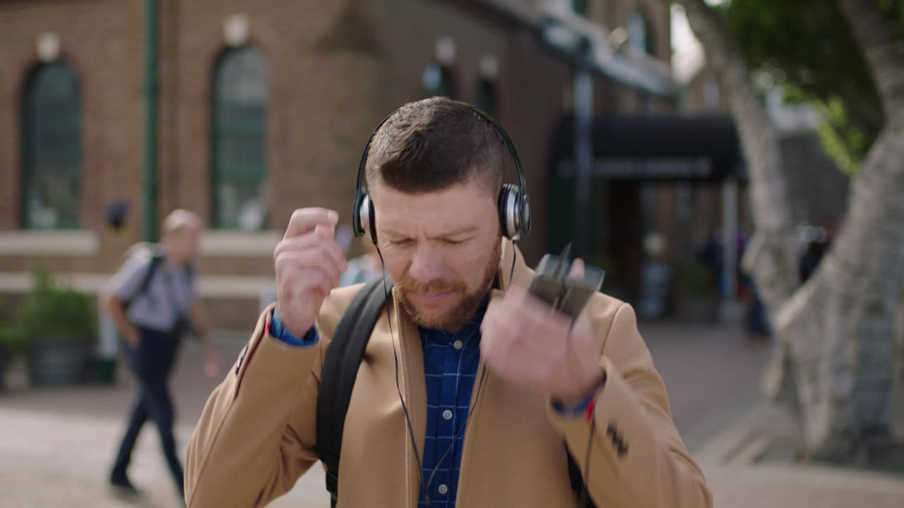 ritratto di un affascinante uomo caucasico che indossa cuffie e ascolta musica usando uno smartphone in città