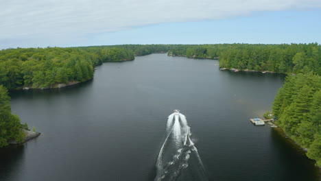 aerial view following a boat with waterskier behind it driving down a river on a summer day, before the waterskier eventually falls