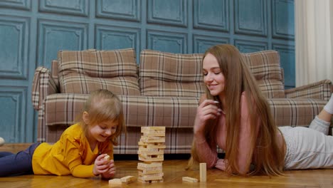 Feliz-Joven-Madre-Enseñando-A-Su-Hija-Pequeña-A-Jugar-Juegos-De-Mesa-Con-Bloques-De-Madera-En-Casa