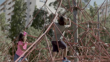 niños caucásicos felices trepando por la cuerda atracción en el patio de recreo