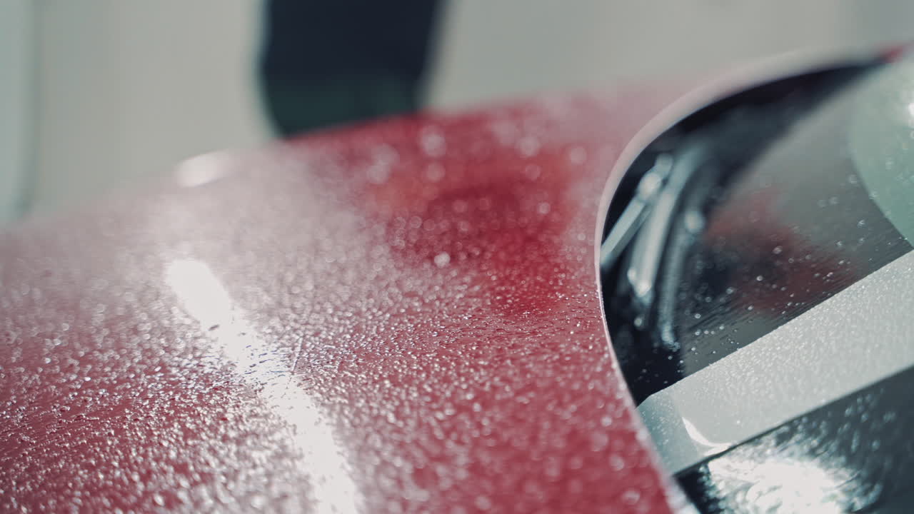 Washer cleaning red car at service station. Close up of hood of modern car covered with foam in car wash