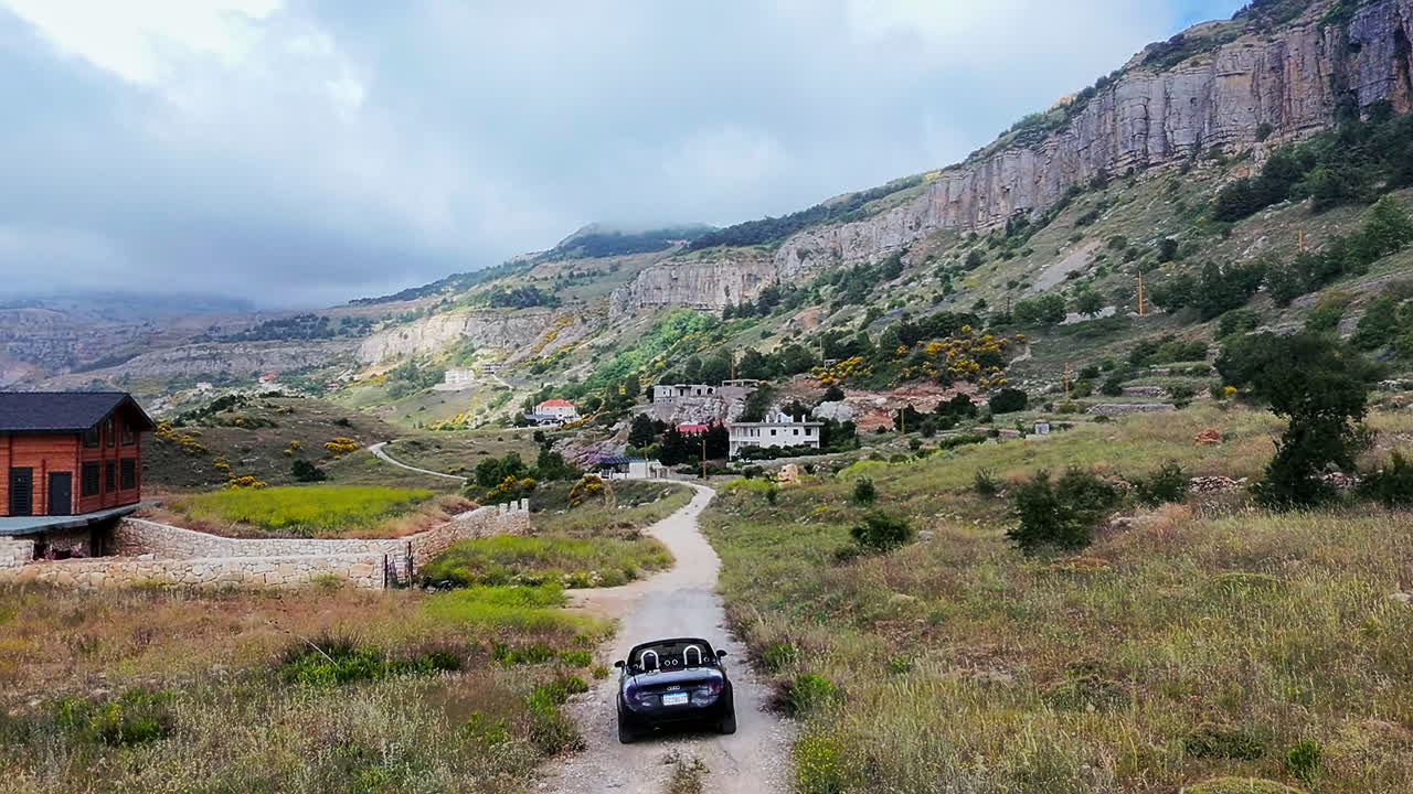Ripresa 'follow me' di un'auto decappottabile nera in corsa su una strada di montagna, Hemmena, Libano.