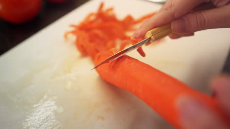 manos femeninas pelando zanahorias en la cocina a cámara lenta