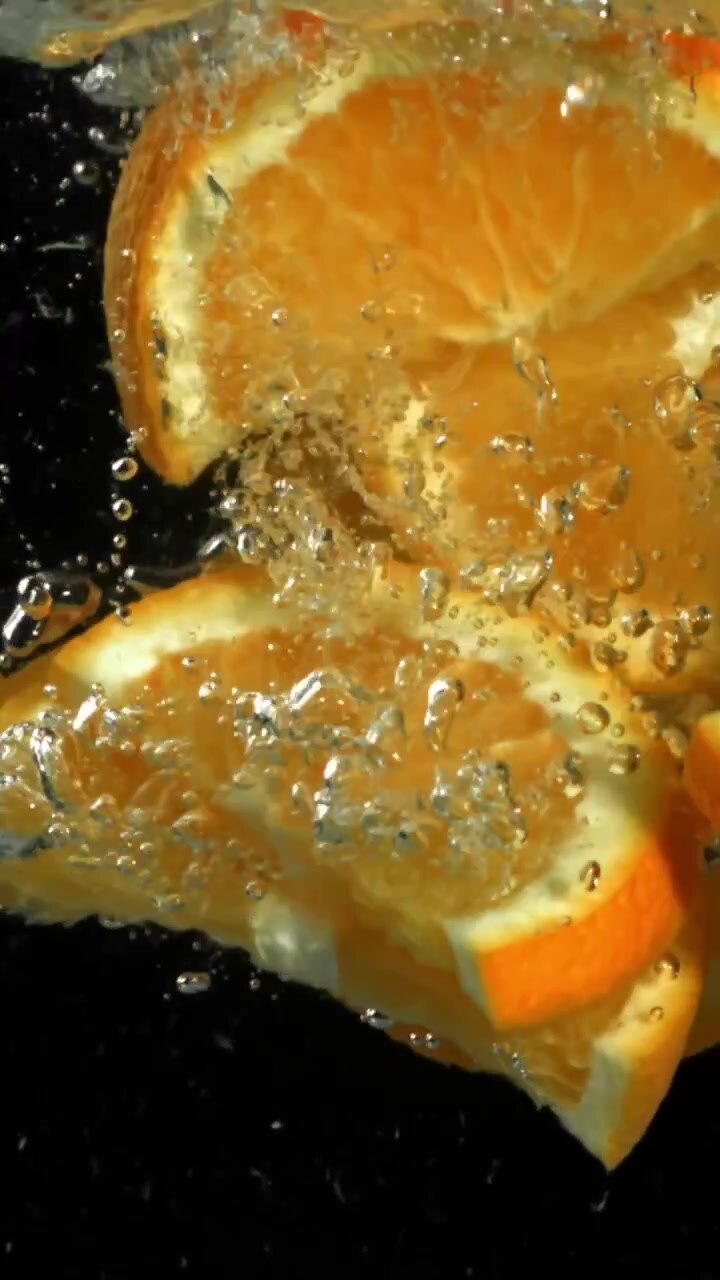 Fette d'arancia al rallentatore che schizzano nell'acqua con bolle