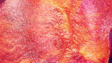 macro shot of glittery orange, yellow, and red inks flowing under air pressure, creating a moving river-like texture of shimmering pigments
