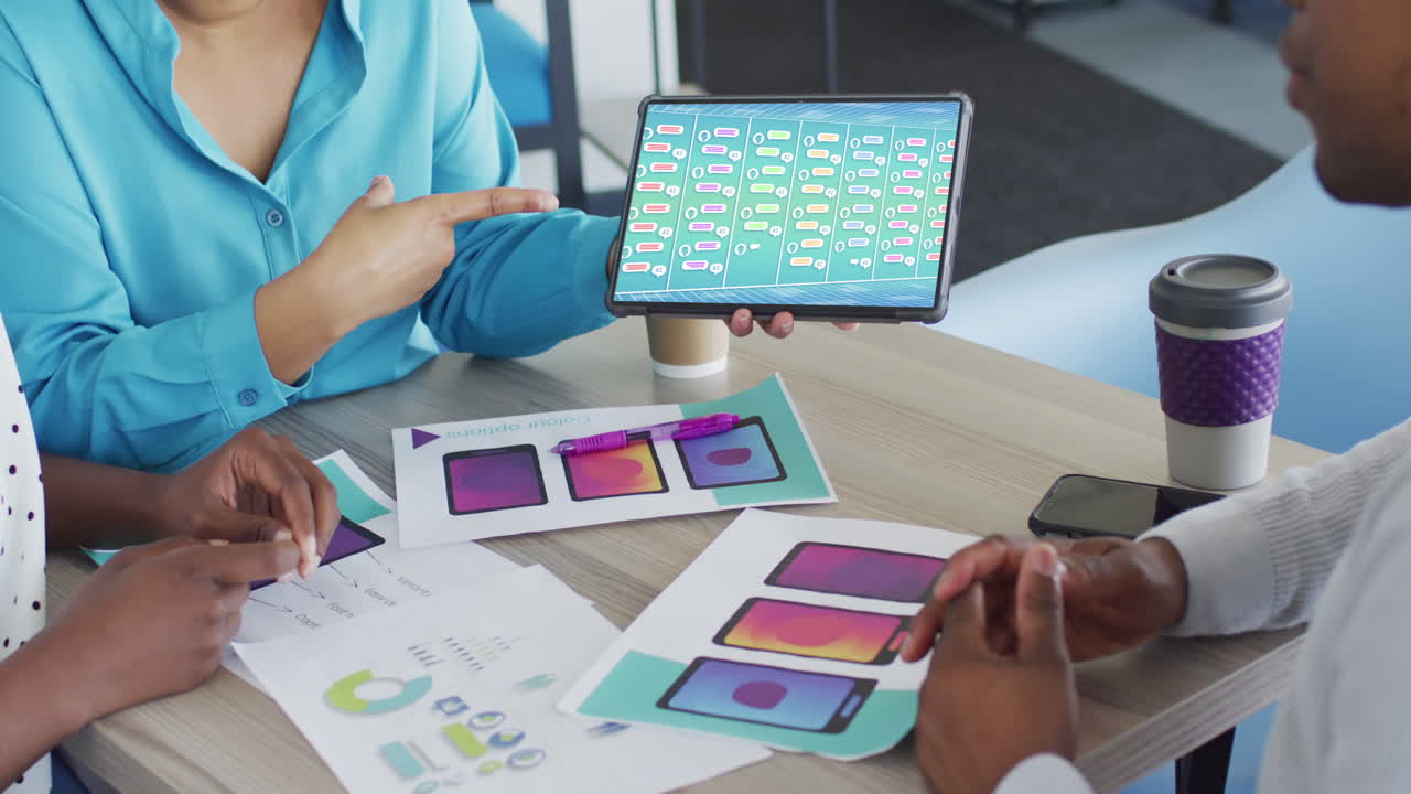 mujer de negocios creativa biracial usando una tableta con datos de mensajes en la pantalla en una reunión de diseño de oficina