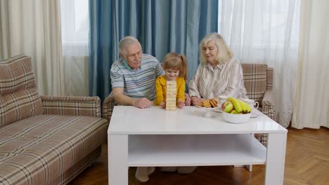 Senior-couple-grandparents-with-child-kid-granddaughter-playing-game-with-wooden-blocks-at-home