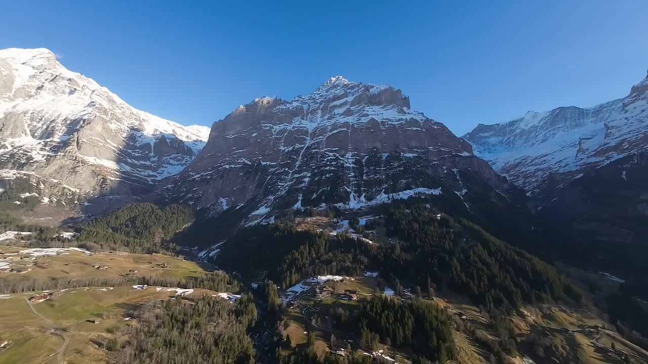 escarpados acantilados de los alpes suizos y el pueblo de grindelwald en un valle sombreado muy por debajo de las cimas nevadas de las montañas