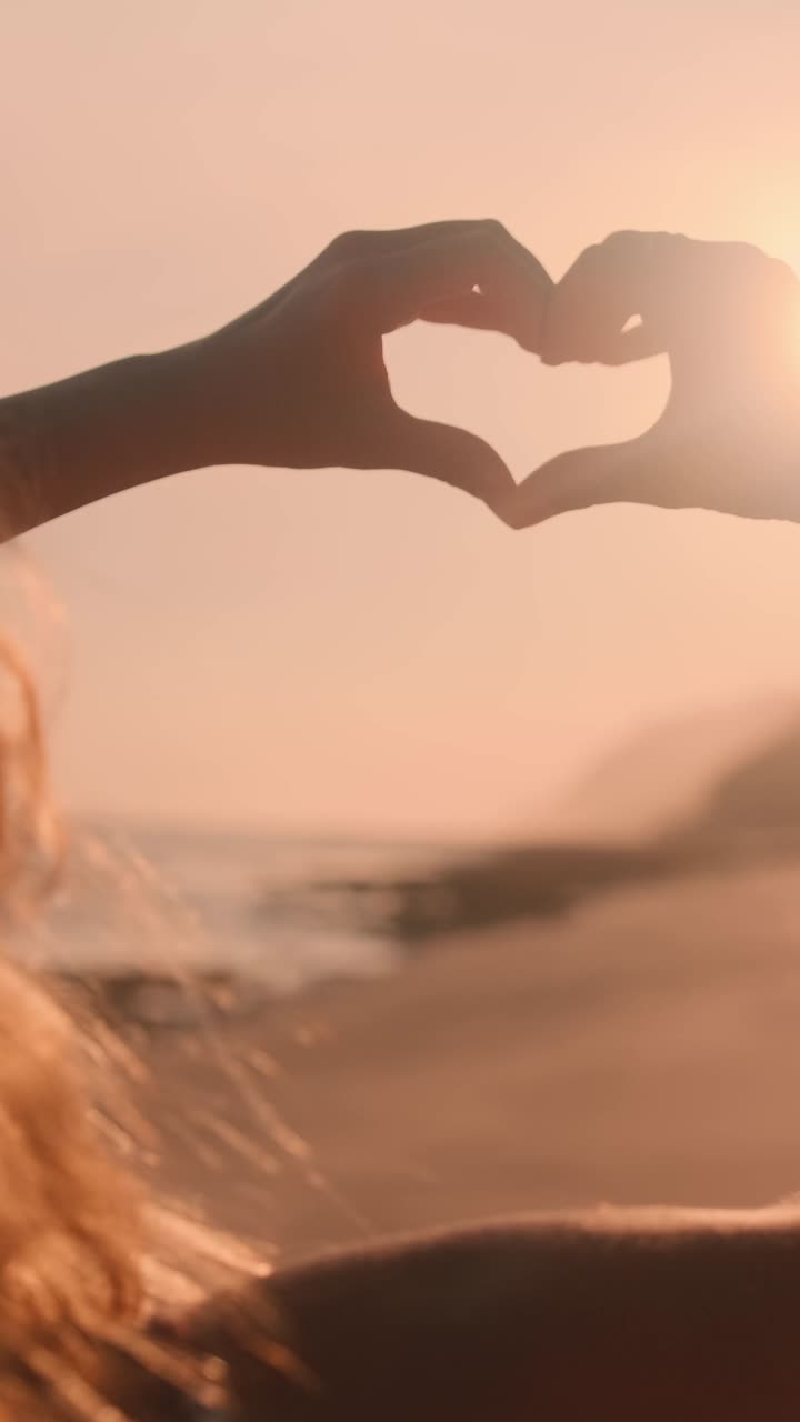 Create a heart shape at sunset with hands at a beautiful beach