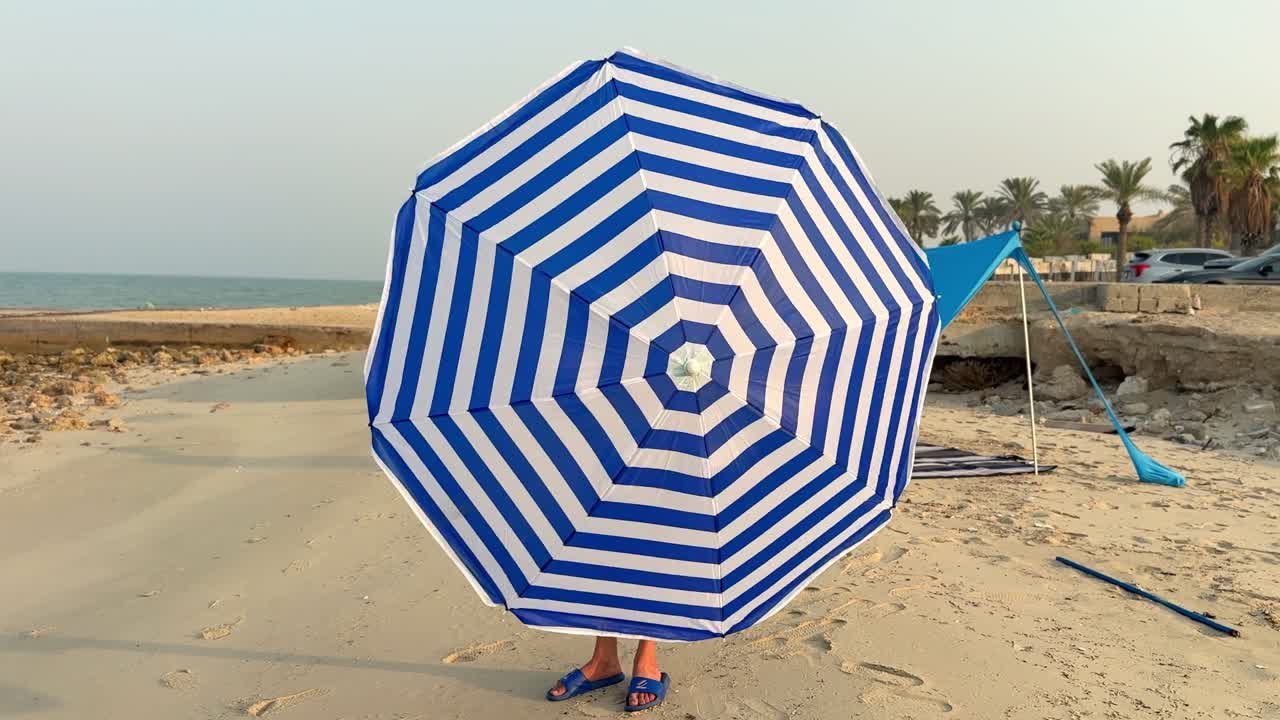 A blue and white striped beach umbrella provides shade on the sandy shore. Perfect for beach vacations, outdoor relaxation, and seaside moments