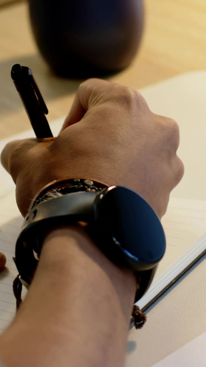 Vertical video: Lowering pen, right arm writing at desk working reaching laptop showing watch beads