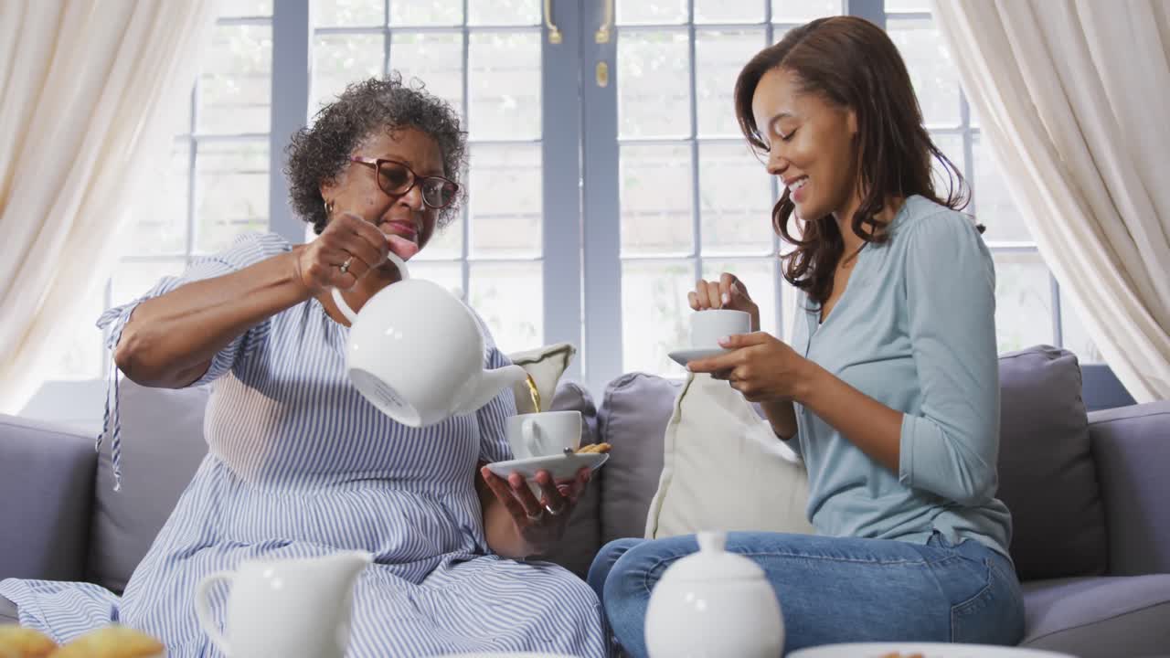 Senior mixed race woman drinking tea with her daughter in social distancing