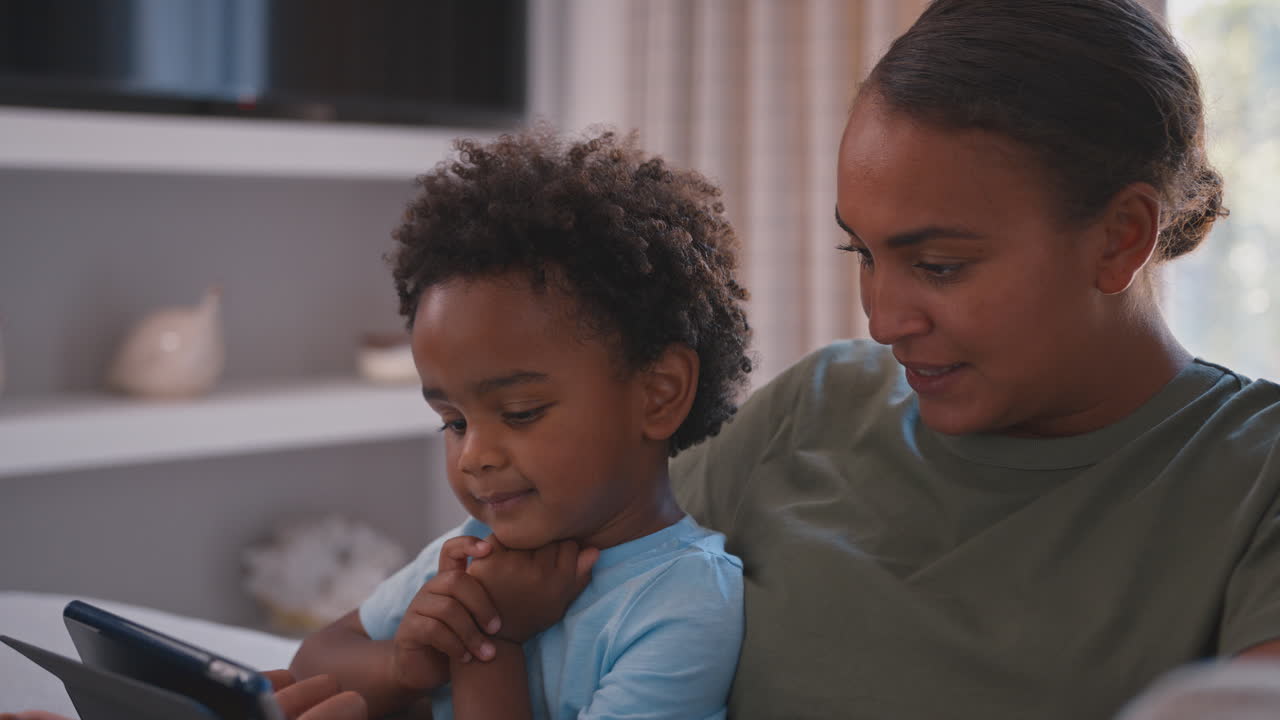 Mother With Son Playing Game Or Streaming To Digital Tablet Sitting On Sofa At Home Together