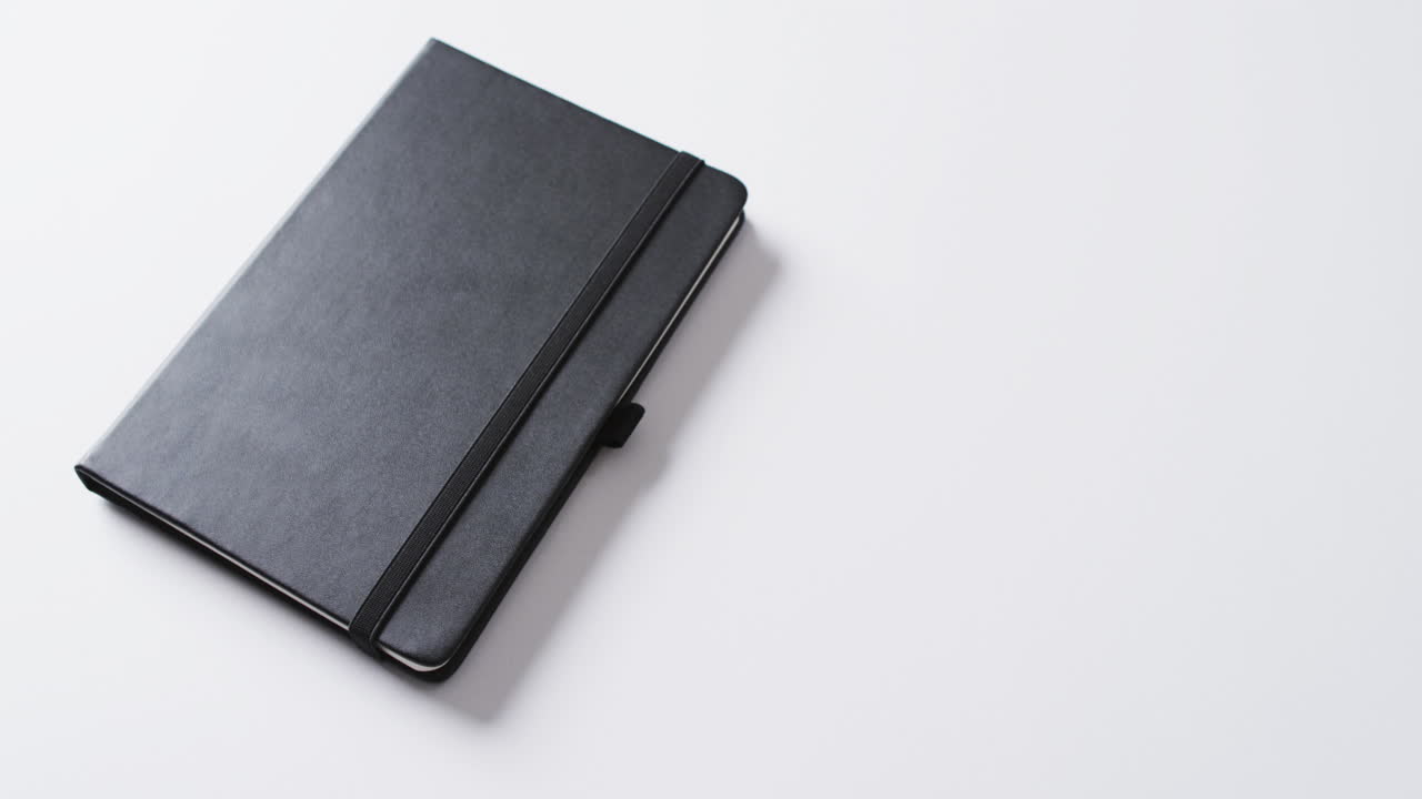 Close up of closed black notebook with copy space on white background in slow motion