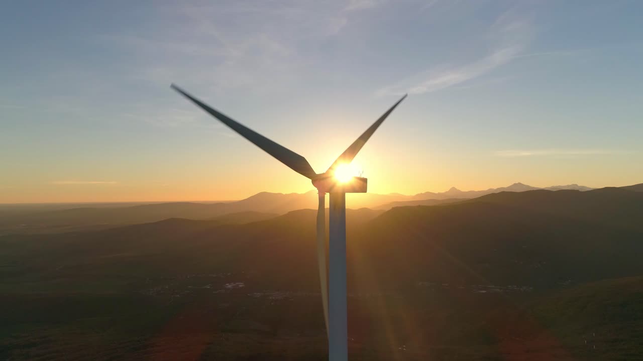 Windmill rotating in front of the sun in the sunset. The propellers cut the sunshine. Aerial shot