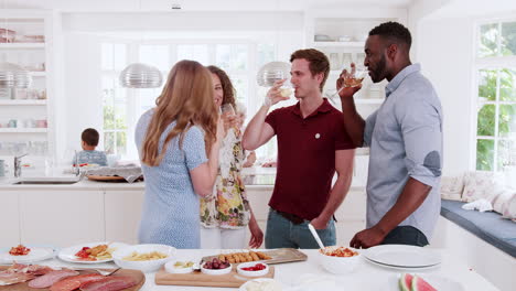 Multi-Generation-Family-And-Friends-Making-A-Toast-In-Kitchen-At-Celebration-Party