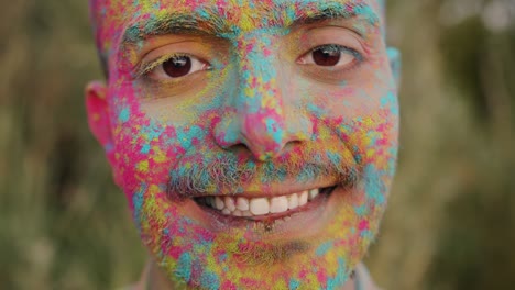 close-up slow motion portrait of handsome arab guy with painted face standing outdoors at holi festival