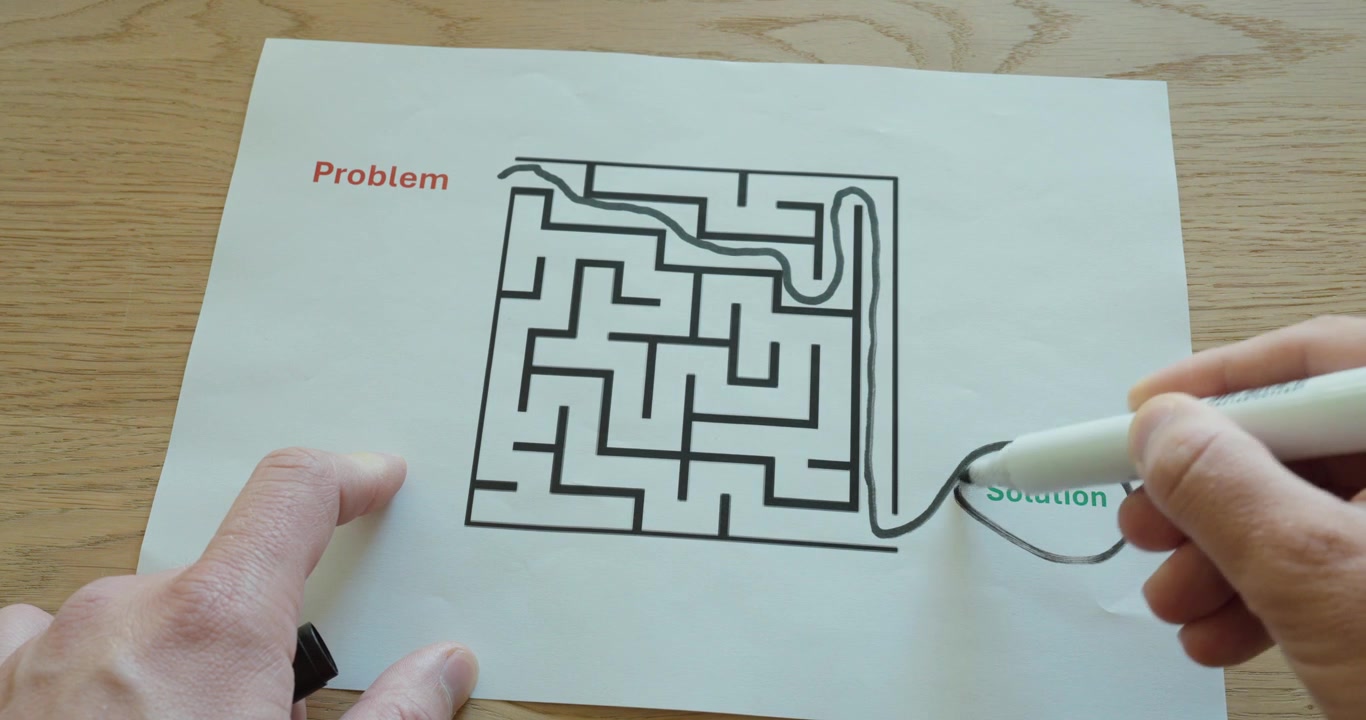 Close-up of hands solving a printed maze labeled problem and solution using a marker. Visual metaphor for problem solving, strategy, decision making, and finding the right path in business or everyday