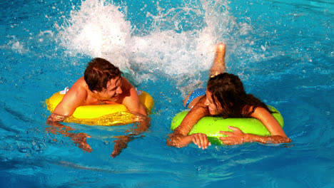 Pareja-Joven-Chapoteando-Y-Divirtiéndose-En-La-Piscina-Con-Anillos-Inflables