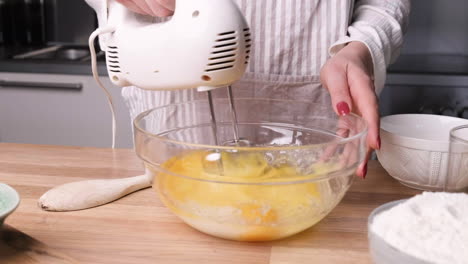 beating eggs and mixing with sugar using electric mixer in a glass bowl