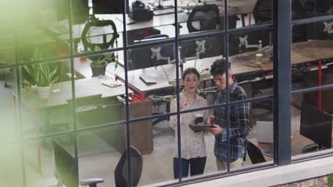 two diverse creative designers in discussion at tablet in casual office, slow motion