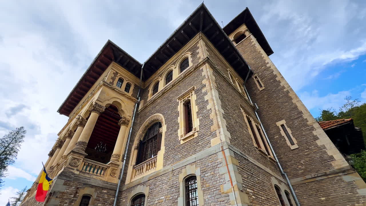 Romanian flag hanging on the brick wall of the old building. Low angle on the beautiful façade of the Cantacuzino Castle, Bu?teni, Romania