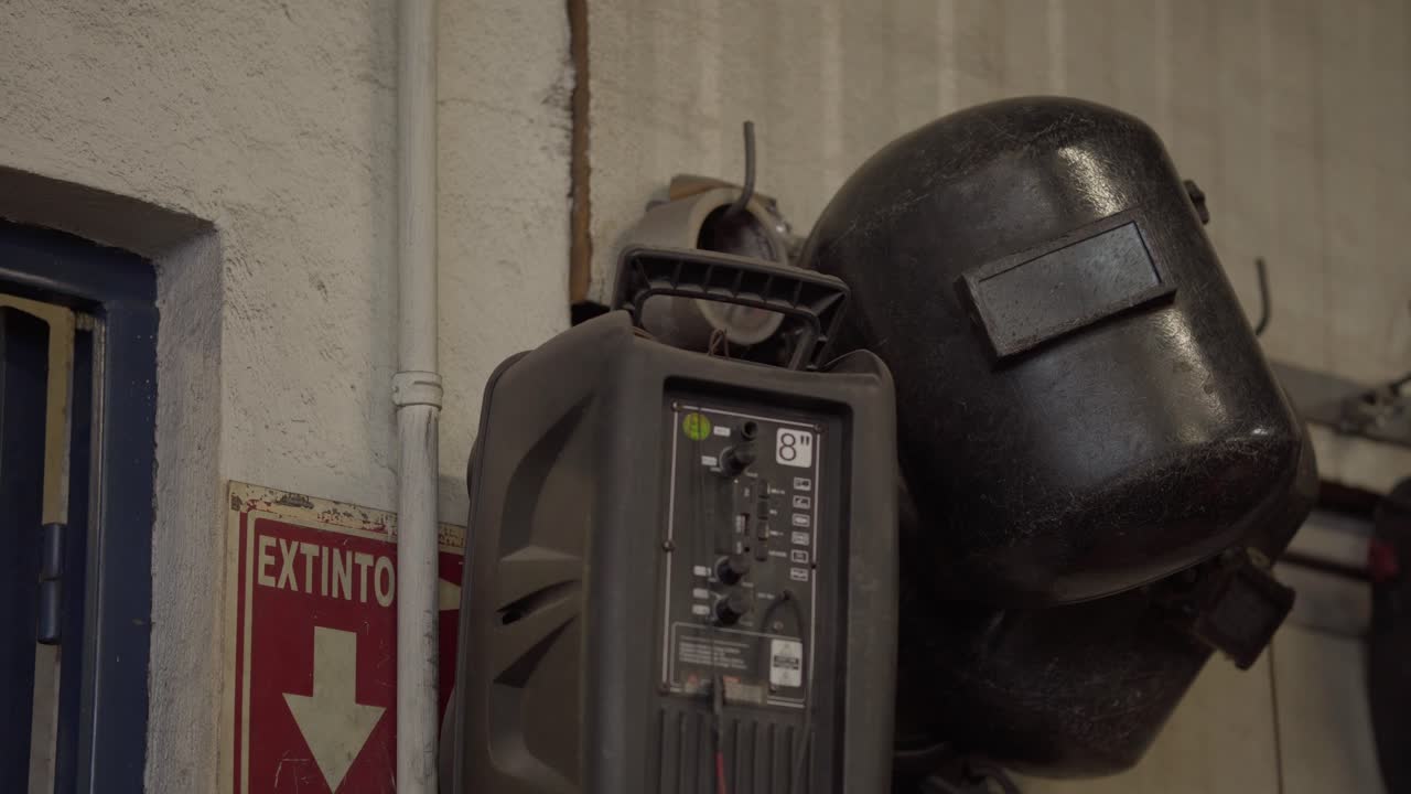 Panning shot showing protective helmets, welding masks, and machinery near fire extinguisher sign