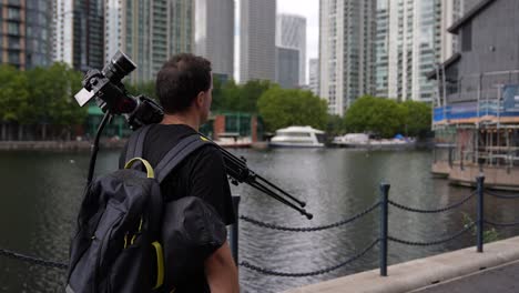 Young-man-is-walking-the-streets-of-London-with-his-camera-on-a-tripod-carrying-on-his-shoulder