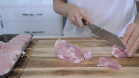 sliding shot of woman in kitchen cutting chicken and vegetables for asian stir fry