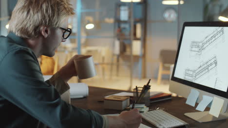 architect drinking coffee and using computer in night office