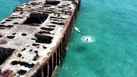 drone aerial view, female person jumping from shipwreck in turquoise sea water