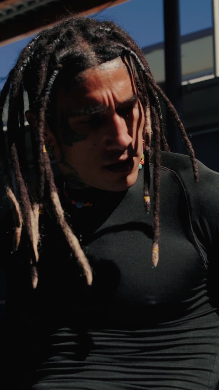 Ung mand med dreadlocks og tatoveringer, der poserer udendørs