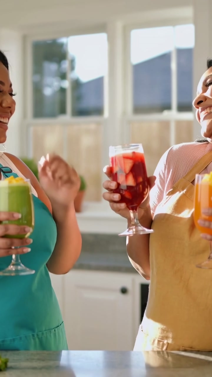 Vertical video: Conversation starting, friends clinking stemmed glasses in kitchen wearing aprons