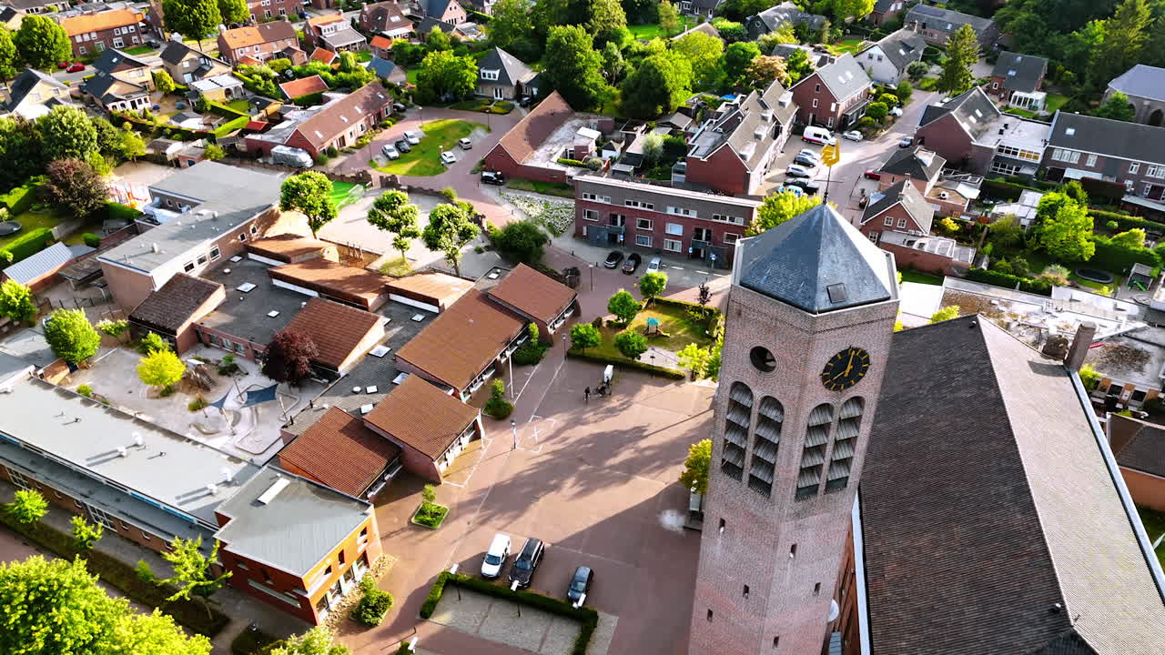Flight around the hexagon clock tower freestanding near the Saint Lawrence Church. Lovely panorama of Vierlingsbeek, Netherlands at backdrop