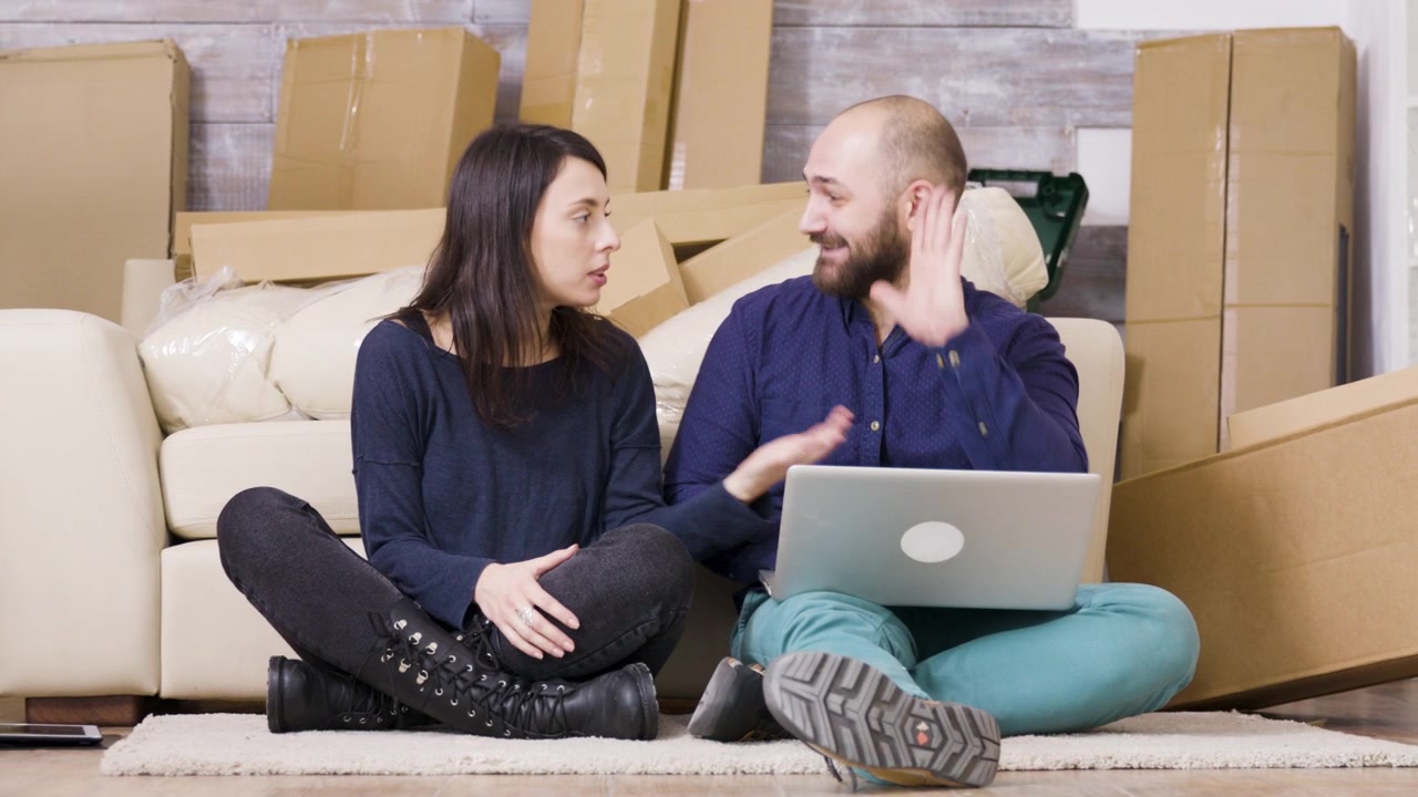 Pareja joven sentada en el suelo usando un portátil en su nuevo apartamento