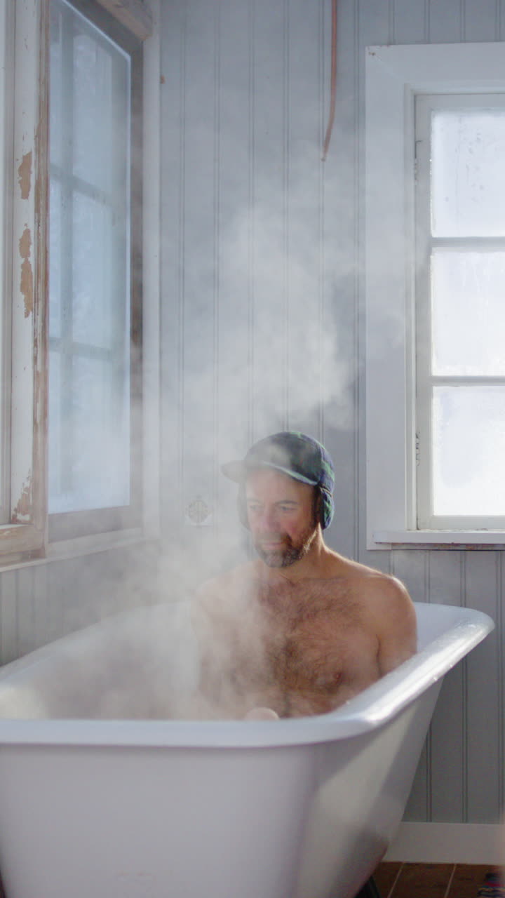 Swedish man climbs into steaming bath in shabby chic room, wellness. Vertical