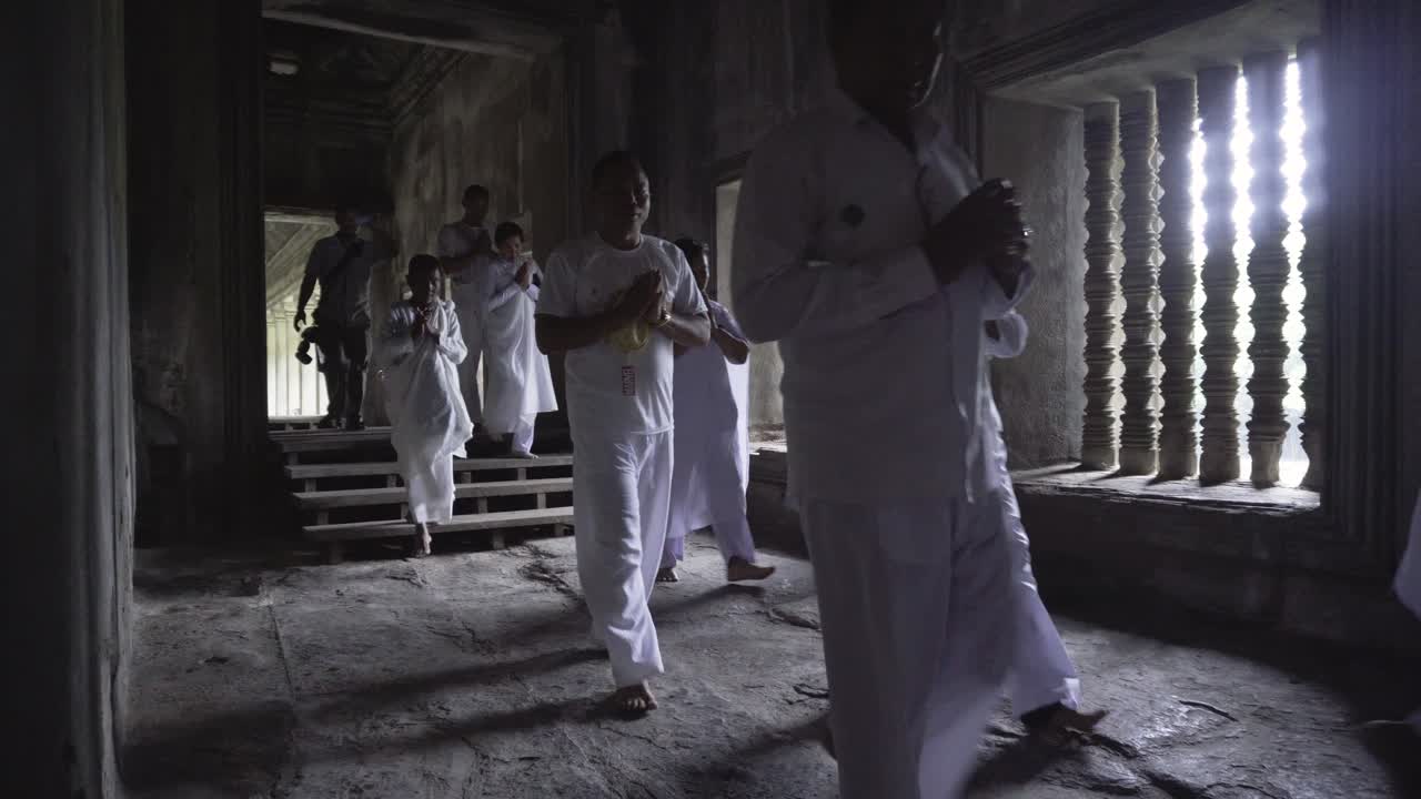 Ley men and women in white robes walking and preying in the galleries of Angkor Wat on their annual buddhist pilgrimage, Cambodia.
