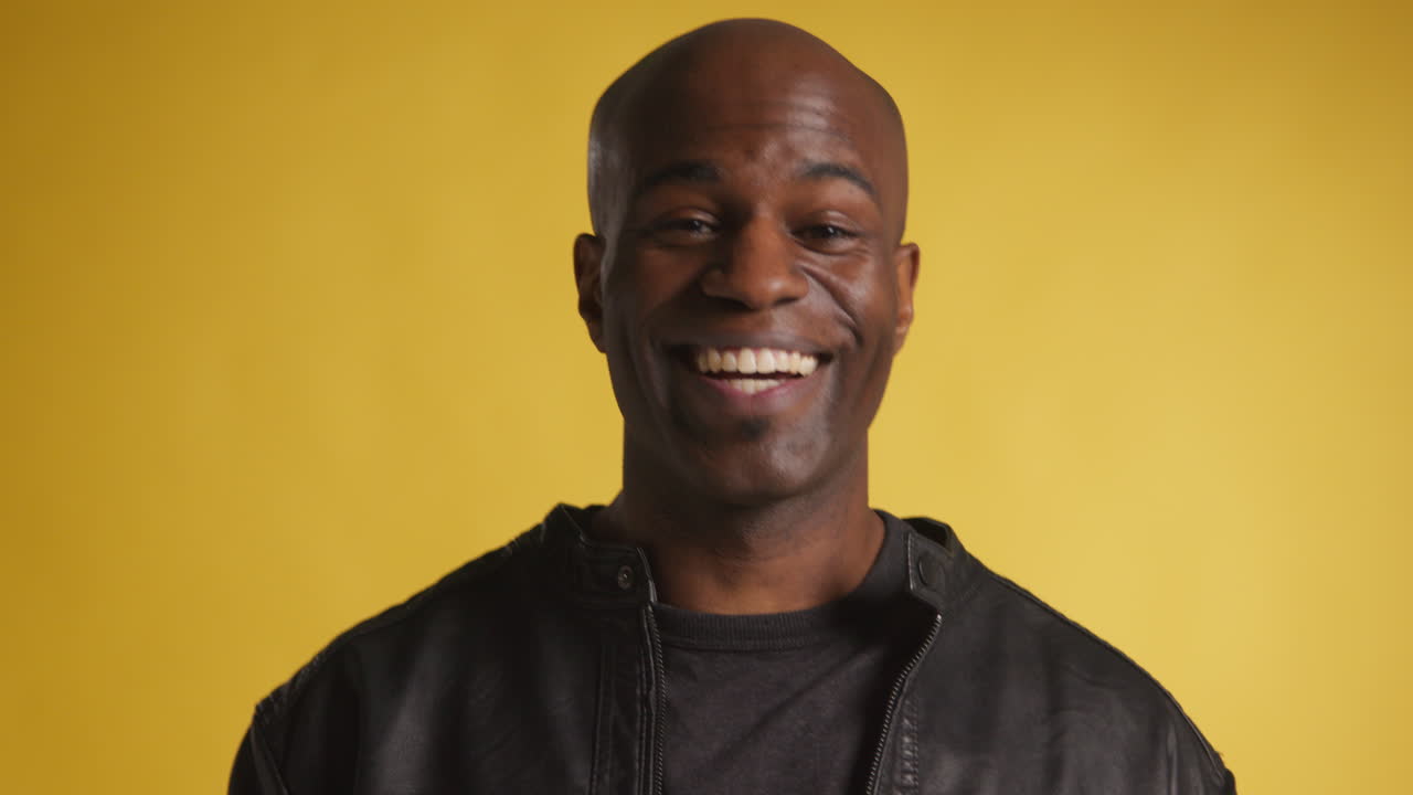 Head And Shoulders Studio Portrait Of Smiling And Laughing Mature Man Against Yellow Background 2
