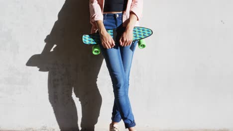 woman with skate board leaning against wall under flyover 4k