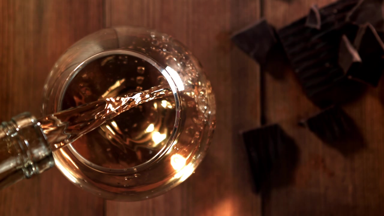 Versamento al rallentatore di distillato ambrato in un bicchiere con cioccolato