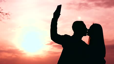 silhouette of a couple kissing and taking a selfie at sunset