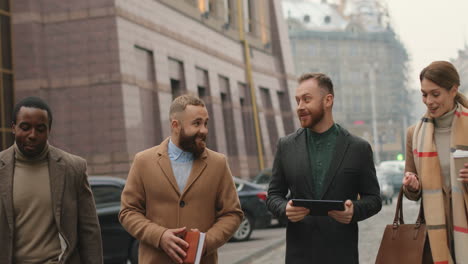 multiethnic business team talking and walking on the street while drinking coffee and using a tablet