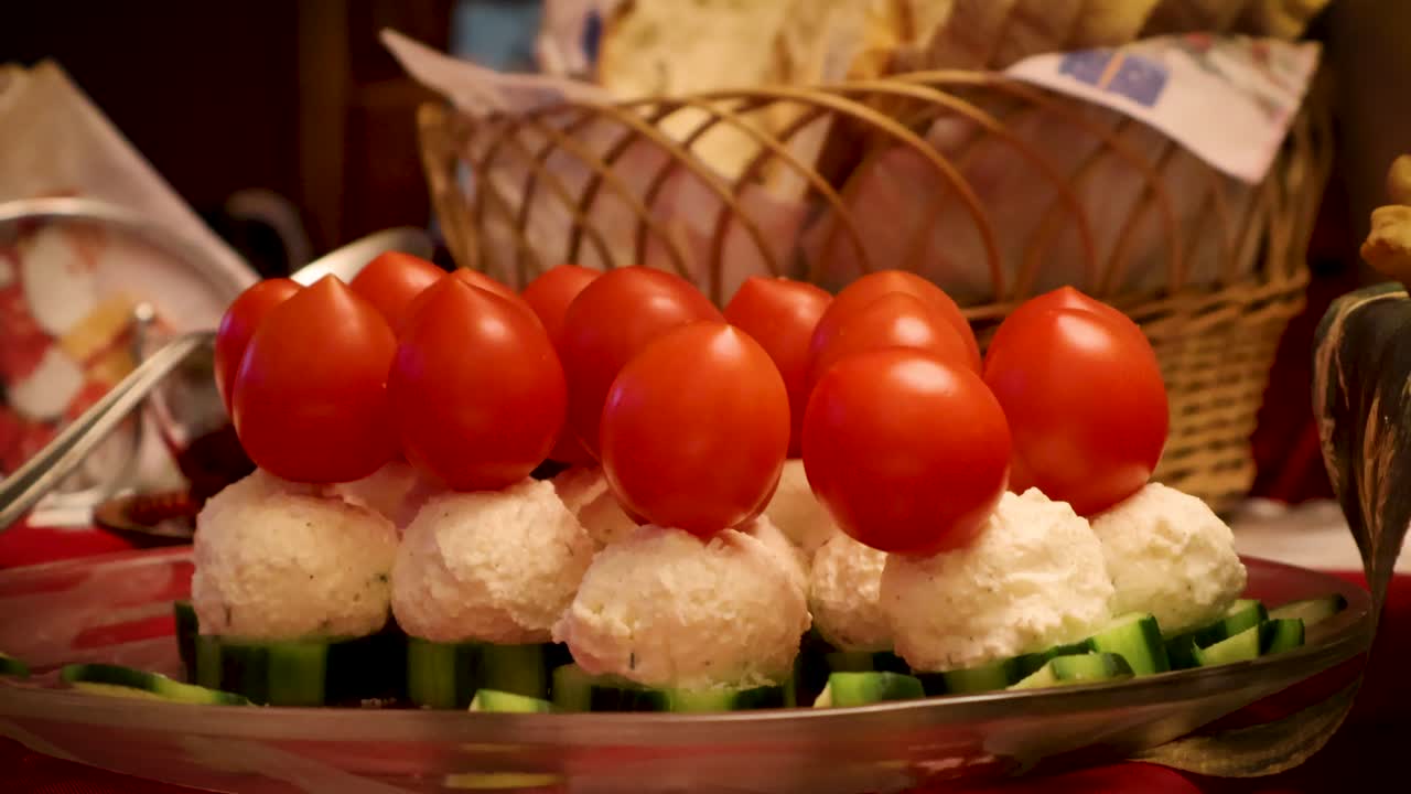 Primo piano di un festoso antipasto rumeno con pomodorini ciliegino su palline di formaggio cremoso adagiate su fette di cetriolo, servito durante una festa in famiglia a un tavolo imbandito a festa