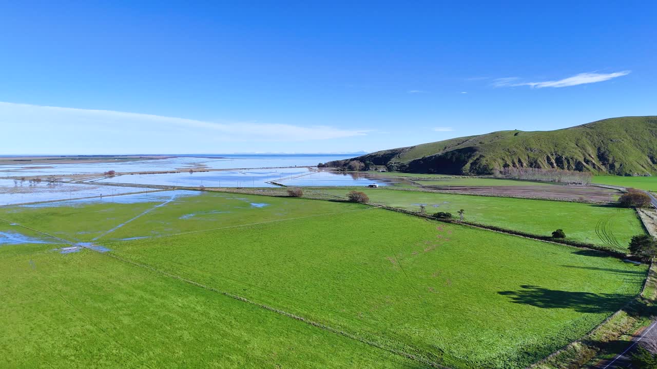 Sweeping aerial footage of vibrant green fields and hills under clear blue skies in Akaroa, New Zealand