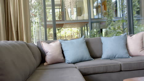 brown couch with pillows, gold curtains and huge windows in sunny living room, slow motion